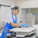 Woman worker in cheese production line at dairy facility wearing protective gear.