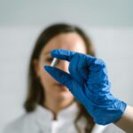 Female scientist in lab coat and gloves examining a capsule in laboratory setting.